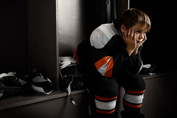 Sad boy in a hockey uniform, looking sad in locker room