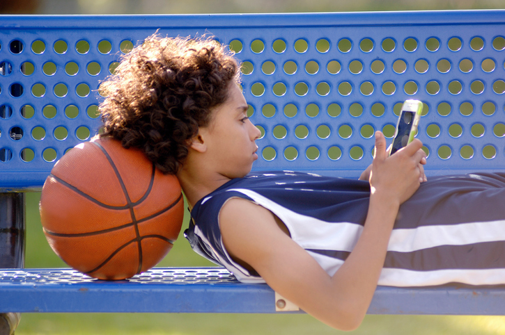 Boy laying on a bench, looking at a cell phone
