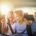Three kids laughing in car on a road trip. Kids are aged 10 and 7. The kids are laughing and embracing, Sunny summer day.