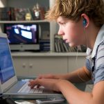 Young boy in bedroom using laptop and listening to MP3 player